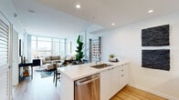 Located at 955 Eleventh Avenue in San Diego's dynamic Little Italy district, this thoughtfully designed one-bedroom, one-bathroom residence offers a sleek, modern living experience. The open-concept floor plan seamlessly connects the kitchen, dining, and living areas, maximizing the sense of space throughout.

The kitchen is outfitted with white flat-panel cabinetry, stainless steel appliances including a French door refrigerator, microwave, range, and dishwasher, complemented by a clean quartz-topped island with an undermount sink. Warm hardwood flooring flows throughout the main living areas, adding natural contrast to the crisp white palette.

The living room is a standout space, anchored by dramatic floor-to-ceiling windows that flood the room with natural light and frame sweeping San Diego skyline views. A private balcony extends from this area, offering direct access to outdoor living. The bedroom features the same warm hardwood flooring, modern sconce lighting, and a sliding door closet.

The bathroom is finished with marble-style tile in the shower and tub surround, a white vanity with an undermount sink, and a mirrored medicine cabinet. An in-unit washer and dryer add everyday convenience. The overall ambiance is clean, contemporary, and urban, ideal for modern city living.