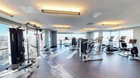 Located on the upper floors of 850 11 St SW in Calgary, Alberta, this fitness centre offers a generously sized, single-floor exercise space designed to support a comprehensive range of workout routines. The room is bathed in abundant natural light, courtesy of expansive floor-to-ceiling windows that wrap around the perimeter and frame sweeping panoramic views of the Calgary skyline and surrounding landscape — a striking backdrop that elevates the overall experience.

The exercise room is thoughtfully outfitted with a diverse selection of commercial-grade equipment. Cardio offerings include multiple treadmills, stationary bikes, ellipticals, and a rowing machine, all positioned to take advantage of the outstanding views. The strength training area features cable machines, a multi-functional weight machine, a power rack with free weights, and adjustable benches, providing ample options for both resistance and functional training.

The space maintains a clean, modern aesthetic with neutral-toned walls, recessed and overhead warm lighting, and durable rubberized flooring suited to high-activity use. The open layout ensures comfortable circulation between equipment stations. The combination of high-elevation city views, well-maintained equipment, and a bright, airy atmosphere makes this fitness centre a well-appointed amenity for building residents.