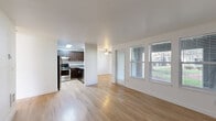 Located in Vancouver, WA, this single-floor 2-bedroom, 2-bathroom unit offers a clean, modern aesthetic throughout. Light wood-look flooring runs continuously across all rooms, complementing the crisp white walls and creating a bright, cohesive feel.

The combined kitchen and living area serves as the heart of the home. The living room features a wood-burning fireplace with a classic white surround and dark tile hearth, flanked by windows that invite natural light. The kitchen is well-appointed with rich dark-stained cabinetry, stainless steel appliances including a refrigerator and range, gray countertops, and a skylight that enhances the sense of openness.

A hallway connects the bedrooms and bathrooms toward the rear of the unit. The primary bedroom is generously proportioned, featuring three large windows with outdoor views of mature trees and greenery, plus a built-in desk. The second bedroom also benefits from multiple windows and a closet. Both bathrooms are consistently finished with dark wood vanities, gray countertops, and full tub-shower combinations. Baseboard heating is present in the bedrooms. A dedicated closet provides additional storage. The overall layout is efficient and well-organized, making practical use of the available space.