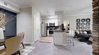 This single-story residence offers a thoughtfully designed layout with a modern aesthetic carried throughout. The open-concept kitchen is a functional highlight, featuring stainless steel appliances including a refrigerator, range, and built-in microwave, complemented by crisp white cabinetry, dark countertops, and a peninsula with bar seating. A herringbone-patterned hard-surface floor extends through the kitchen and living areas, adding visual interest underfoot.

The living room is bright and inviting, benefiting from a large window that draws in natural light and provides outdoor views. Crown molding and a ceiling fan contribute to the room's polished character. A defined dining area features a dark accent wall paired with a textured wall art piece, creating an intimate setting for meals.

The bedrooms are carpeted for comfort, each offering closet storage—one featuring mirrored sliding doors—and windows that let in natural light. The bathroom includes a full tub-shower combination with tile surround and herringbone flooring consistent with the rest of the unit. A dedicated in-unit laundry area with side-by-side washer and dryer and overhead shelving adds everyday convenience throughout this well-rounded residence.