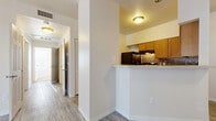 This single-floor residence offers a thoughtfully designed layout that balances comfort and functionality. The kitchen is a standout feature, equipped with warm oak cabinetry, a mosaic tile backsplash, light countertops, black appliances including a range and dishwasher, and a generous peninsula breakfast bar with a built-in sink — ideal for both meal preparation and casual dining. Wood-style plank flooring runs through the main living and kitchen areas, adding a clean, cohesive look throughout.

A hallway connects the living spaces to the bedrooms, which feature plush carpeting and an abundance of natural light through large windows fitted with blinds. One bedroom includes a ceiling fan and light fixture, enhancing comfort year-round. Another room opens to the outdoors through a sliding glass door dressed with vertical blinds, offering a seamless transition to an exterior space.

The bathroom is well-proportioned, featuring wood-toned cabinetry, a single vanity with a mirror and overhead lighting, a toilet, and wood-look tile flooring. The overall palette throughout the residence is neutral and bright, with white walls and trim creating a clean, airy atmosphere. A louvered closet door in the hallway adds a practical storage element to the thoughtful design.