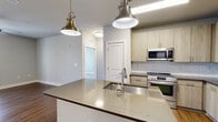 This thoughtfully designed 2-bedroom, 2-bathroom single-floor residence offers a functional and modern layout across a comfortable footprint. The open-concept kitchen is a standout feature, boasting light wood cabinetry, quartz countertops, a subway tile backsplash, stainless steel appliances including a refrigerator, range, and microwave, and a large island with an undermount sink illuminated by stylish brass pendant lights. Wood-look flooring runs throughout the main living areas, complementing the neutral gray walls and clean white trim.

The primary bedroom is a well-sized retreat with hardwood-style flooring, large windows offering outdoor views, and access to a private en-suite bathroom. The en-suite features a dual-sink vanity with light wood cabinetry, dark countertops, and a glass-enclosed walk-in shower with white subway tile. The second bedroom features plush carpet, ample natural light from a large window, and a well-sized closet with wire shelving. The second bathroom mirrors the primary in style, featuring a soaking tub with subway tile surround and a single vanity. A dedicated laundry room houses a full-size washer and dryer, adding everyday convenience to this move-in-ready home.