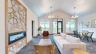 This generously sized clubroom in De Forest, Wisconsin offers a thoughtfully designed community space spread across a single floor. The layout encompasses a welcoming hallway, a spacious living area, and a dedicated room, all connected by wide, carpeted corridors adorned with a curated gallery of framed artwork and stylish pendant and sputnik-style light fixtures.

The living room serves as the social centerpiece, featuring a striking floor-to-ceiling stone fireplace framed in warm wood, vaulted shiplap ceilings, and an inviting arrangement of sofas and mid-century modern accent chairs. Large windows flood the space with natural light and offer views of the surrounding landscape. Adjacent seating nooks and dining-style tables with booth seating provide additional gathering options.

Transparency and openness define the workspace area, where glass-enclosed conference rooms with sleek sliding doors allow for private meetings while maintaining visual connectivity to the broader space. A counter-height work bar positioned beside oversized windows creates an ideal spot for focused work bathed in daylight.

The private room features soft sage-green walls, a rattan accent chair, and curated wall art, offering a serene retreat. Throughout, patterned carpeting, warm wood baseboards, and a cohesive modern-casual design palette unify every zone of this versatile, community-focused clubroom.