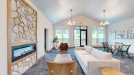 This generously sized clubroom in De Forest, Wisconsin offers a thoughtfully designed community space spread across a single floor. The layout encompasses a welcoming hallway, a spacious living area, and a dedicated room, all connected by wide, carpeted corridors adorned with a curated gallery of framed artwork and stylish pendant and sputnik-style light fixtures.

The living room serves as the social centerpiece, featuring a striking floor-to-ceiling stone fireplace framed in warm wood, vaulted shiplap ceilings, and an inviting arrangement of sofas and mid-century modern accent chairs. Large windows flood the space with natural light and offer views of the surrounding landscape. Adjacent seating nooks and dining-style tables with booth seating provide additional gathering options.

Transparency and openness define the workspace area, where glass-enclosed conference rooms with sleek sliding doors allow for private meetings while maintaining visual connectivity to the broader space. A counter-height work bar positioned beside oversized windows creates an ideal spot for focused work bathed in daylight.

The private room features soft sage-green walls, a rattan accent chair, and curated wall art, offering a serene retreat. Throughout, patterned carpeting, warm wood baseboards, and a cohesive modern-casual design palette unify every zone of this versatile, community-focused clubroom.