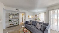 This single-story, one-bedroom, one-bathroom residence offers a thoughtfully designed layout that makes efficient use of its space. The open-concept living and dining area serves as the heart of the home, featuring plush carpeting, a textured ceiling, and large windows that invite an abundance of natural light. A sliding glass door connects the living area to an outdoor patio, offering views of the surrounding greenery. The kitchen is positioned adjacent to the living space and features warm wood cabinetry, granite-style countertops, a built-in range, and a tall window that brightens the galley-style workspace. Hardwood-style flooring runs through the kitchen and into the dedicated laundry room, which is equipped with a full-size washer and dryer alongside built-in shelving for additional storage. The bedroom is a comfortable retreat with carpeted flooring, a ceiling fan, and a large window fitted with sheer curtains that allow soft, diffused light to fill the room. A closet provides convenient storage. The bathroom includes a granite-top vanity with a wide mirror, a shower-tub combination, and floating shelves for organized storage. Throughout the residence, a neutral color palette and consistent finishes create a cohesive and inviting ambiance.