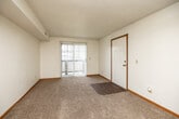 This single-floor unit offers a straightforward, functional layout with neutral finishes throughout. The living area is carpeted in a warm beige tone and features a textured ceiling, wood-trimmed baseboards, and a sliding glass door that opens to a private balcony, allowing natural light to fill the space and providing outdoor views. A hard-surface entry area at the threshold transitions into the carpet, creating a practical entryway.

The kitchen is equipped with a coil-burner electric range, a refrigerator, wood-toned cabinetry, and dark laminate countertops. An overhead ventilation hood is positioned above the range, and the cabinetry provides ample storage.

The bedrooms are carpeted and finished with the same neutral palette. One bedroom benefits from two windows overlooking greenery, while another features a single window with a blind, both allowing generous natural light. The textured ceilings are consistent throughout.

The bathroom includes a full-size tub and shower combination with a white surround, a toilet, and wood-look flooring, offering a clean and utilitarian design. Overall, the unit presents a practical, move-in-ready space with consistent finishes and a calm, neutral ambiance.