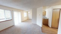 Located in Poulsbo, Washington, this single-floor unit offers a practical and comfortable layout designed for everyday living. The open-concept living and dining area is bright and welcoming, featuring plush carpeting, a ceiling fan, and large sliding glass doors that invite natural light. A brick-surround fireplace serves as a focal point in the living room, adding warmth and character to the space. Baseboard heating is present throughout, ensuring consistent comfort year-round. The kitchen is efficiently designed with light wood cabinetry, ample counter space, a stainless steel sink, and white appliances including a refrigerator, range, and dishwasher. Hardwood-style flooring in the kitchen transitions smoothly from the carpeted living areas. The unit includes multiple bedrooms, each carpeted and equipped with windows that allow in natural light and views of the surrounding neighborhood. Textured ceilings are featured throughout the unit, giving the interior a consistent finish. The overall layout, visible in the dollhouse view, demonstrates a well-organized floor plan with clear separation between the kitchen, living spaces, and private rooms, making this a functional and livable space in the heart of Poulsbo.