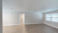 This single-floor space is finished in a clean, neutral palette throughout, creating a cohesive and move-in-ready atmosphere. The open living area is anchored by light wood-look plank flooring, soft gray walls, and bright white trim, lending the space a fresh, contemporary feel. A doorway leads directly to a bathroom accessible from the main living area, adding practical convenience.

An adjacent dining or secondary living space continues the wood-look flooring and benefits from natural light through multiple windows fitted with horizontal blinds. A passthrough connects to the kitchen, which features white cabinetry, granite-look countertops with brushed hardware, and a stainless steel refrigerator—offering a modern, functional workspace.

The bedrooms are carpeted in warm beige tones and each include ceiling light fixtures and windows that bring in natural light. The bathroom is well-appointed with a full soaking tub and a subway tile surround in a classic brick pattern, complemented by wood-look flooring. A hallway with adjacent closet space connects the kitchen to the bedroom wing. The overall layout is efficient and thoughtfully designed, with consistent finishes throughout.