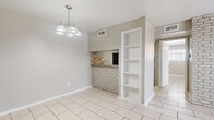 Located at 7637 Harwin Dr in Houston, TX, this single-story, one-bedroom, one-bathroom unit offers a practical and well-organized layout across a comfortable footprint. Light-toned large-format tile flooring runs throughout, creating a cohesive and easy-to-maintain interior.

The open living and dining area is bright and spacious, featuring a white-painted exposed brick accent wall that adds character and texture. A pendant chandelier illuminates the dining space, which connects seamlessly to the kitchen via a pass-through counter with a matching brick surround and a mosaic tile backsplash. The kitchen is equipped with white cabinetry, granite-style countertops, and black appliances including an electric range and refrigerator. A built-in shelving unit adjacent to the kitchen provides additional storage and display space.

The bedroom is generously sized, receiving natural light through a window with blinds and featuring a ceiling fan overhead. Two closets offer ample storage, and direct access to the bathroom is conveniently located within the room.

The bathroom includes a vanity with a granite-style countertop, a tub-shower combination, and tile flooring with a decorative border detail. A hallway connects the main living areas to the private quarters, completing this functional and neatly appointed home.