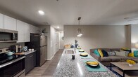 This well-appointed single-floor residence offers a thoughtfully designed open-concept layout that seamlessly connects the kitchen, dining, and living areas. The kitchen is a standout feature, showcasing a large granite-topped island with an undermount sink, pendant lighting, and seating for multiple guests. Two-toned cabinetry — with light upper cabinets and dark lower cabinets — pairs with a full suite of stainless steel appliances, including a refrigerator, range, and over-the-range microwave. Wood-style flooring runs throughout the main living areas, adding warmth and continuity. The living space is bright and welcoming, with a glass-panel entry door that brings in natural light. Two comfortable bedrooms each feature ceiling fans, windows with blinds, and soft carpeting. Both bathrooms mirror the kitchen's design aesthetic, with dark vanity cabinetry, granite countertops, and well-lit vanity mirrors. A hallway with louvered closet doors provides practical storage throughout. The overall ambiance is modern and cohesive, combining neutral warm tones with contemporary finishes to create a comfortable and functional living environment.