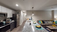 This well-appointed single-floor residence offers a thoughtfully designed open-concept layout that seamlessly connects the kitchen, dining, and living areas. The kitchen is a standout feature, showcasing a large granite-topped island with an undermount sink, pendant lighting, and seating for multiple guests. Two-toned cabinetry — with light upper cabinets and dark lower cabinets — pairs with a full suite of stainless steel appliances, including a refrigerator, range, and over-the-range microwave. Wood-style flooring runs throughout the main living areas, adding warmth and continuity. The living space is bright and welcoming, with a glass-panel entry door that brings in natural light. Two comfortable bedrooms each feature ceiling fans, windows with blinds, and soft carpeting. Both bathrooms mirror the kitchen's design aesthetic, with dark vanity cabinetry, granite countertops, and well-lit vanity mirrors. A hallway with louvered closet doors provides practical storage throughout. The overall ambiance is modern and cohesive, combining neutral warm tones with contemporary finishes to create a comfortable and functional living environment.