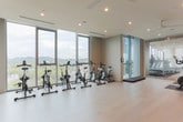 Located in Nashville, TN, this contemporary fitness facility is thoughtfully designed to deliver a premium workout experience across a single, well-appointed floor. The space is divided into distinct functional zones, each finished with clean, modern aesthetics characterized by light hardwood-style flooring, crisp white walls, and recessed lighting throughout.

The spin studio is a dedicated room housing a row of stationary cycling bikes positioned directly in front of expansive floor-to-ceiling windows. These windows flood the room with natural light and frame sweeping panoramic views of Nashville's rolling hills and cityscape, creating an immersive and motivating environment.

An open multi-purpose exercise area serves as the central hub of the facility. This airy space features a ceiling fan, recessed lighting, and a large wall-mounted mirror with a ballet barre, making it well-suited for stretching, yoga, or group fitness classes. A pass-through window connects this area to an adjacent viewing or monitoring room, adding a functional architectural detail.

A glassed-in cardio room is accessible through a sleek sliding glass door and houses treadmills and additional cardio equipment. The transparent enclosure maintains visual openness throughout the facility. An outdoor balcony area adjacent to the space provides access to fresh air and further unobstructed views of the Nashville skyline and surrounding landscape, enhancing the overall wellness-focused atmosphere of this upscale fitness center.