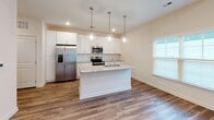This single-floor residence is designed with a clean, modern aesthetic and an open layout that promotes a sense of spaciousness throughout. The kitchen serves as a central highlight, outfitted with white shaker cabinetry, granite countertops, and a full suite of stainless steel appliances including a French door refrigerator with ice maker, electric range, and built-in microwave. A white subway tile backsplash adds a crisp, contemporary touch, while a center island with an integrated sink and pendant globe lighting above provides both functionality and visual appeal. The kitchen flows seamlessly into the main living area, which features warm wood-look flooring, vaulted ceilings, and French doors that open to an outdoor deck, filling the space with natural light. A bathroom offers a granite-topped vanity with an undermount sink and brushed nickel fixtures. A carpeted bedroom provides a softer, quieter retreat, complete with a two-panel interior door. Recessed lighting throughout and a neutral color palette of soft whites and warm beiges give the entire home a bright, cohesive, and welcoming ambiance.