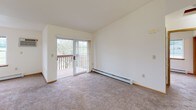 Located at 897 Arthur Dr in Milton, Wisconsin, this single-floor unit offers a practical and well-organized layout designed for comfortable everyday living. The kitchen is equipped with warm oak cabinetry providing ample storage, white appliances including a refrigerator, dishwasher, and electric range, and light vinyl flooring. A pendant light fixture illuminates the space, and a pass-through counter connects the kitchen to the adjacent living area. The living room features plush carpeting, a ceiling fan, and a sliding glass door that opens onto a wooden balcony overlooking a tree-lined outdoor setting, bringing in natural light and pleasant views. A separate carpeted bedroom benefits from two windows on adjacent walls, filling the room with natural light and views of the surrounding greenery, along with baseboard heating for year-round comfort. The full bathroom includes a tub-shower combination, toilet, vanity, and tile-patterned vinyl flooring. A dedicated laundry area houses a full-size washer and dryer alongside a water heater, with shelving above for added storage. Throughout the unit, neutral wall tones and light wood trim create a clean, cohesive aesthetic.