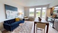 This well-designed single-floor residence offers a thoughtful layout that balances comfort and functionality. The open-concept living and dining area serves as the heart of the home, featuring light hardwood flooring, crisp white walls, and large windows that flood the space with natural light and frame tranquil views of lush greenery. The living area is anchored by a plush navy blue sofa, a soft shag area rug, and a bold abstract wall painting, creating an inviting and stylish atmosphere. A dining table positioned near the expansive windows makes for a bright and pleasant place to gather.

The kitchen is outfitted with sleek, dark wood cabinetry extending floor to ceiling, light countertops, and a full suite of stainless steel appliances including a refrigerator, electric range, built-in microwave, and dishwasher. Recessed lighting and easy-care hardwood flooring complete the modern aesthetic.

The bedroom offers a calm retreat, highlighted by a soft blue accent wall, plush carpeting, a double closet with sliding doors, and tasteful framed artwork. The bathroom is finished with warm wood-tone cabinetry, a white countertop, light hardwood-style flooring, and clean, neutral walls, delivering a fresh and polished feel throughout.