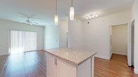 This well-appointed single-floor residence offers a thoughtfully designed open-concept layout that seamlessly connects the kitchen, dining, and living areas. The kitchen is a standout feature, showcasing crisp white shaker-style cabinetry extending to the ceiling, granite countertops, and a full suite of stainless steel appliances including a French door refrigerator with ice maker, electric range, built-in microwave, and dishwasher. A central kitchen island with matching granite surface and pendant lighting serves as both a functional workspace and a natural gathering point. Track lighting illuminates the adjoining living area, which benefits from elevated ceilings and a ceiling fan, creating an airy and comfortable atmosphere. Warm hardwood-style flooring flows consistently throughout the main living spaces, adding richness and cohesion to the interior. The bedroom is generously proportioned, featuring a ceiling fan, a large window with blinds that admits ample natural light, and the same durable flooring. The bathroom is finished with neutral tile flooring, a granite-topped vanity, and a clean white color palette. A dedicated in-unit laundry area with a full-size washer and dryer adds everyday convenience. The overall design is modern, clean, and functional.