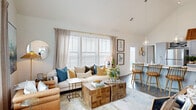 Located at 406 Ledbury Rd in Wilmington, NC, this single-floor, 2-bedroom, 2-bathroom home offers a well-designed layout with thoughtful finishes throughout. The open-concept living and kitchen area is the heart of the home, anchored by soaring vaulted ceilings that amplify the sense of space. The living room features large windows with plantation shutters that flood the area with natural light, complemented by hardwood-style flooring that runs throughout. The kitchen is equipped with stainless steel appliances, soft gray shaker-style cabinetry, white quartz countertops, and a spacious island with seating — ideal for both everyday living and entertaining. A sliding door offers access to a private outdoor patio area. The generously sized primary bedroom includes a dedicated closet and an en-suite bathroom featuring a dual-sink vanity with gray cabinetry, white quartz countertops, and a glass-enclosed walk-in shower. The second bedroom is bright and comfortable, served by a well-appointed second bathroom with matching design elements. Two closets, a hallway, and a welcoming entrance complete the thoughtfully arranged floor plan, making this home both functional and visually cohesive.