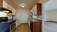 This single-floor unit offers a practical and straightforward layout designed for comfortable everyday living. The galley-style kitchen is well-equipped, featuring a stainless steel electric range, white refrigerator, and dishwasher. Rich wood-toned upper cabinetry contrasts with white lower cabinets, complemented by dark laminate countertops and a double-basin sink. Durable tile flooring runs throughout the kitchen, adding to its functional character.

The living area is generously sized, finished with wall-to-wall carpeting and neutral white walls that create a clean, open feel. A large sliding glass door floods the space with natural light and provides direct access to an outdoor balcony, extending the living area to the outdoors. A wall-mounted air conditioning unit ensures year-round comfort.

Two bedrooms are carpeted and feature windows that bring in natural light, along with baseboard heating that runs along the perimeter walls for efficient warmth. The full bathroom includes a single-sink vanity with cabinet storage below, a tiled floor in a classic geometric pattern, and a full tub-shower combination. Throughout the unit, wood-trimmed doors and warm-toned accents provide a cohesive, understated aesthetic.