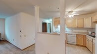 This single-floor unit offers a practical and comfortable layout designed for everyday living. The open living and dining area is generously sized, finished with neutral wall-to-wall carpeting, and anchored by an elegant chandelier overhead. A wall-unit air conditioner and baseboard heating ensure year-round comfort, while a large window invites natural light and views of the surrounding neighborhood.

The kitchen is positioned adjacent to the living area, separated by a half-wall partition that maintains an open feel while defining the cooking space. Warm oak cabinetry lines the walls, providing ample storage alongside light-toned countertops. A ceiling fan with light fixture, a white refrigerator, an electric range with overhead exhaust hood, and a double-basin sink complete the kitchen's functional setup. The tile flooring is easy to maintain and contrasts neatly with the carpeted living spaces.

The bedrooms are calm and well-proportioned, each featuring plush carpeting, neutral walls, and windows with blinds that offer outdoor views and natural light, complemented by baseboard heating beneath each window.

The bathroom is clean and functional, featuring a full-size soaking tub with a shower rod, a single-sink vanity with an oak cabinet base, a large mirror, and stone-look tile flooring that ties the space together with a classic aesthetic.