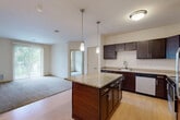 Located at 1300 Post Rd in Fitchburg, Wisconsin, this two-bedroom, one-bathroom unit offers a thoughtfully designed single-floor layout that makes efficient use of its space. The open-concept kitchen and living area serves as the heart of the home, where rich dark-wood cabinetry, granite countertops, a central island with pendant lighting, and stainless steel appliances — including a range, microwave, and dishwasher — combine to create a functional and attractive kitchen. Light wood-style flooring anchors the kitchen, transitioning into plush carpeting in the living area, which features a sliding glass door that fills the room with natural light and provides direct access to a private patio overlooking a landscaped, tree-lined neighborhood. The primary bedroom is generously sized and includes a walk-in closet with wire shelving, while the second bedroom offers carpeted flooring and a window with outdoor views. Four closets in total provide exceptional storage throughout. The full bathroom is well-appointed with dual sinks, dark wood cabinetry, a large mirror, and wood-look flooring. A dedicated laundry area adds everyday convenience. Neutral tones and clean finishes throughout lend the space a calm, move-in-ready aesthetic.