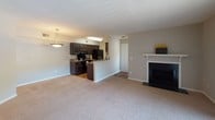 Located at 101 Bridgetown Rd in Goose Creek, South Carolina, Unit 8H is a single-floor residence thoughtfully designed for comfortable living. The open-concept layout connects the living area and kitchen, creating a spacious and functional common space. The living room features plush neutral carpeting, a classic white-mantled fireplace with a black surround, and a sliding glass door dressed with vertical blinds that allows abundant natural light and outdoor access. A pendant light fixture adds a decorative touch to the transition between the living and kitchen areas. The kitchen is well-equipped with rich dark espresso cabinetry, granite-style countertops, hardwood-style flooring, and black appliances including a range and refrigerator. A breakfast bar provides additional prep and seating space. The bedrooms are carpeted and filled with natural light from windows with blinds; one includes a ceiling fan with light fixture. The bathroom features a vanity with a granite-style countertop and an undermount sink, complemented by hardwood-style flooring and a bifold closet door for added storage. Throughout the unit, neutral gray walls and textured ceilings provide a clean, cohesive aesthetic that is both inviting and move-in ready.