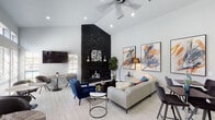 Located at 5728 Remington Cir in Fort Worth, TX, this single-story community clubhouse delivers a polished, contemporary aesthetic throughout its well-appointed interior. The space is anchored by a striking floor-to-ceiling stacked black stone fireplace that rises dramatically beneath soaring vaulted ceilings, creating an impressive focal point in the main lounge area. Light wood-look tile flooring flows consistently throughout, complementing the bright white walls and recessed lighting that keep the space feeling open and airy. A ceiling fan adds comfort to the vaulted lounge, where bold abstract artwork in blue and orange tones adds a vibrant, curated character to the walls. The reception area features a skylight that floods the room with natural light, a long white service counter with multiple workstations, and a seating arrangement anchored by a colorful area rug. French doors with geometric glass pane detailing provide a welcoming entrance. A casual café-style seating zone lines a wall of tall windows with transom panels above, allowing abundant natural light and offering a relaxed space for smaller gatherings. A self-serve beverage station is conveniently positioned nearby. Together, these distinct zones create a versatile, well-designed communal space ideal for both social interaction and everyday convenience.