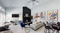 Located at 5728 Remington Cir in Fort Worth, TX, this single-story community clubhouse delivers a polished, contemporary aesthetic throughout its well-appointed interior. The space is anchored by a striking floor-to-ceiling stacked black stone fireplace that rises dramatically beneath soaring vaulted ceilings, creating an impressive focal point in the main lounge area. Light wood-look tile flooring flows consistently throughout, complementing the bright white walls and recessed lighting that keep the space feeling open and airy. A ceiling fan adds comfort to the vaulted lounge, where bold abstract artwork in blue and orange tones adds a vibrant, curated character to the walls. The reception area features a skylight that floods the room with natural light, a long white service counter with multiple workstations, and a seating arrangement anchored by a colorful area rug. French doors with geometric glass pane detailing provide a welcoming entrance. A casual café-style seating zone lines a wall of tall windows with transom panels above, allowing abundant natural light and offering a relaxed space for smaller gatherings. A self-serve beverage station is conveniently positioned nearby. Together, these distinct zones create a versatile, well-designed communal space ideal for both social interaction and everyday convenience.