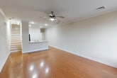 Located at Railroad Plaza in Bay Shore, NY, this well-appointed 1-bedroom, 2-bathroom unit spans two floors, offering a functional and comfortable layout. The main level features a generous open-concept living, dining, and kitchen area bathed in natural light from large windows flanking the front entry door, which includes a transom window above. Warm hardwood flooring flows throughout, complemented by crown molding and a ceiling fan with light fixture. The kitchen is equipped with rich wood cabinetry, granite-style countertops, a peninsula with an integrated sink, and black appliances including a gas range, built-in microwave, and refrigerator. Recessed lighting enhances the kitchen's functionality. A staircase with wood treads leads to the upper level, where the spacious primary bedroom offers plush carpeting, a closet, and natural light through double windows with exterior views. Two full bathrooms — one featuring a tiled tub/shower combo — serve the unit. Additional highlights include in-unit laundry and a dedicated closet for storage, rounding out a practical and well-designed living space in a convenient Bay Shore location.