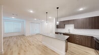 Located at 6519 Kings Glen Drive in Humble, Texas, this single-story, 3-bedroom, 2-bathroom home offers a clean, modern aesthetic with thoughtfully selected finishes throughout. The open-concept kitchen and living area serves as the heart of the home, anchored by a large granite-topped island beneath two sleek pendant lights. Dark wood cabinetry provides a bold contrast against crisp white walls, while stainless steel appliances — including a range, microwave, and refrigerator — complete the well-equipped kitchen. Light wood-style flooring flows throughout the main living areas, complementing the bright, neutral palette. The living room features a glass-panel door that fills the space with natural light. Each bedroom is carpeted for comfort and includes ceiling fans and window blinds. The spacious primary bedroom connects to a walk-in closet outfitted with built-in shelving and hanging rods. Both bathrooms echo the home's modern design with granite vanity tops, wood-toned cabinetry, and light wood flooring. The primary bath includes a walk-in glass shower, while the secondary bath offers a tub-shower combination with tile surround. Recessed lighting throughout ensures a consistently bright and welcoming atmosphere.
