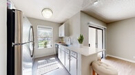 This single-floor residence offers four bedrooms and one bathroom within a thoughtfully arranged layout. The kitchen is a standout feature, finished with crisp white cabinetry, light quartz countertops, stainless steel appliances including a refrigerator and dishwasher, and a peninsula breakfast bar. A window above the counter fills the space with natural light and provides a view of the surrounding greenery. A sliding glass door leads to a compact outdoor storage area with shelving. The bedrooms are uniformly appointed with light wood-style vinyl flooring, soft neutral wall tones, and textured ceilings. Each room receives natural light through blinded windows, creating a bright and airy atmosphere. The shared bathroom is well-equipped with a dual-sink vanity featuring quartz countertops, modern fixtures, a large mirror, and a bathtub/shower combination. Common areas benefit from the same warm flooring that runs throughout the home, lending a cohesive feel to the interior. A ceiling fan is visible in the living area, and the open sightlines between the living space and kitchen enhance the overall sense of flow and connectivity within the home.