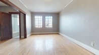 This single-floor space showcases a compelling mix of classic craftsmanship and everyday practicality. Throughout the unit, warm-toned hardwood floors extend seamlessly from room to room, reflecting natural light and contributing to an inviting, open ambiance. Crown molding runs consistently along the ceilings, adding a refined architectural touch to each space.

The main living areas are generously proportioned, with soft grey walls and large multi-pane windows that allow abundant natural light to filter in. A wall-mounted split air conditioning unit ensures year-round comfort. The rooms connect through elegant dark-stained solid wood doorways, some framed by distinctive arched openings that lend the space a timeless character.

The entryway is a standout feature, presenting two graceful arched passageways alongside rich, dark oak doors and trim work — a nod to the building's heritage architecture. A closet or storage area is accessible through one of the arched openings, adding practical utility to the classic aesthetic.

The bathroom is thoughtfully appointed with full white subway tile walls, a classic black-and-white mosaic tile floor, a soaking tub, pedestal sink, and a multi-pane window that brings in natural light. The overall design of this space balances historic charm with clean, functional living.