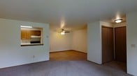 Located at 3220-3224 Mary St in Marinette, Wisconsin, this single-story space offers a straightforward and functional layout designed for comfortable everyday living. The main living area is generously proportioned, finished with wall-to-wall carpeting that adds warmth underfoot, and features a ceiling fan with integrated lighting to ensure year-round comfort and air circulation. Neutral-toned walls throughout lend a clean, versatile backdrop suitable for a variety of interior styles. A pass-through window connects the living area directly to the kitchen, creating an open and communicative flow between spaces. The kitchen is equipped with warm wood-toned cabinetry providing ample storage, and includes built-in appliances such as a range and overhead microwave or ventilation unit. The pass-through counter also serves as a convenient breakfast bar or serving ledge. A hallway visible from the living area leads to additional rooms, suggesting a practical and well-organized floor plan. The overall ambiance is bright, clean, and unpretentious, making this space a solid and livable option in the Marinette community.