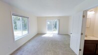 This two-story home features 2 bedrooms and 1.5 bathrooms, offering a practical and comfortable layout spread across two levels. The main living area is finished with neutral wall tones and plush carpeting, creating a warm and inviting atmosphere throughout. Large windows allow abundant natural light to fill the space, enhancing the open, airy feel of the interior. A sliding glass door provides direct access to the outdoors, seamlessly connecting the living area to the exterior and allowing views of the surrounding greenery. The clean, simple architectural lines and light color palette contribute to a bright and understated aesthetic. The half bathroom on the main level adds everyday convenience, while the full bathroom serves the upper floor. The two bedrooms offer private retreats, suitable for rest or use as a home office. Overall, the home presents a straightforward, functional design with well-maintained finishes and a layout that maximizes usability across both floors, making it a practical living space with a calm and comfortable ambiance throughout.