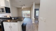 Located at Asbury Square in Dunwoody, Georgia, this single-floor, one-bedroom, one-bathroom residence offers a thoughtfully designed layout that maximizes comfort and functionality. The open-plan living and kitchen area is finished with durable wood-style flooring, neutral-toned walls, and a ceiling fan with light fixture. Sliding glass doors lead to a private balcony framed by lush tree canopy, filling the living space with natural light and verdant outdoor views. The kitchen is well-equipped with white cabinetry, dark granite countertops, stainless steel appliances including a gas range, dishwasher, microwave, and refrigerator, along with a stainless steel sink. The bedroom features plush carpeting, a large window with wooded views, a textured ceiling, and access to a dedicated closet. The bathroom is appointed with wood-style flooring, a soaking tub and shower combination with white subway tile accents and a curved curtain rod, a toilet, and a vanity with mirror. Neutral tones and consistent finishes throughout create a clean, cohesive ambiance suited for comfortable everyday living in a serene, tree-lined setting.