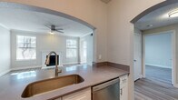 This two-story home offers a thoughtfully organized layout across two floors, with the garage and entryway on the ground level and the main living areas above. A carpeted staircase leads up from the entrance to the primary floor, where light-toned luxury vinyl plank flooring flows throughout the living spaces, complemented by neutral gray walls and crisp white trim.

The open-plan kitchen and living room serves as the heart of the home. The kitchen features stainless steel appliances — including a full-size refrigerator, electric range, over-the-range microwave, and dishwasher — paired with white cabinetry, a subway tile backsplash, and a countertop peninsula with a deep single-basin sink. An elegant arched passthrough connects the kitchen to the living room, which is highlighted by a classic white-mantled fireplace, a ceiling fan, textured ceiling, and multiple windows that invite natural light.

The bedroom offers a comfortable retreat with a window overlooking the exterior and a ceiling fan overhead. The bathroom includes a full soaking tub with a tiled surround. Additional conveniences include a dedicated laundry area with a top-loading washer, a closet, and a hallway connecting the rooms. The attached garage provides secure parking and extra storage space.
