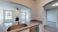 This two-story home offers a thoughtfully organized layout across two floors, with the garage and entryway on the ground level and the main living areas above. A carpeted staircase leads up from the entrance to the primary floor, where light-toned luxury vinyl plank flooring flows throughout the living spaces, complemented by neutral gray walls and crisp white trim.

The open-plan kitchen and living room serves as the heart of the home. The kitchen features stainless steel appliances — including a full-size refrigerator, electric range, over-the-range microwave, and dishwasher — paired with white cabinetry, a subway tile backsplash, and a countertop peninsula with a deep single-basin sink. An elegant arched passthrough connects the kitchen to the living room, which is highlighted by a classic white-mantled fireplace, a ceiling fan, textured ceiling, and multiple windows that invite natural light.

The bedroom offers a comfortable retreat with a window overlooking the exterior and a ceiling fan overhead. The bathroom includes a full soaking tub with a tiled surround. Additional conveniences include a dedicated laundry area with a top-loading washer, a closet, and a hallway connecting the rooms. The attached garage provides secure parking and extra storage space.