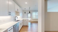 This well-designed 1-bedroom, 1-bathroom unit offers a thoughtful layout that maximizes its compact footprint. Warm wood-look flooring flows throughout the space, creating a cohesive and inviting atmosphere. The open-concept kitchen is a standout feature, showcasing white shaker cabinetry with matte black hardware, a white subway tile backsplash, light quartz countertops, and a full suite of stainless steel appliances including a refrigerator, range, over-the-range microwave, and dishwasher. A peninsula with pendant lighting connects the kitchen seamlessly to the living and dining area, which is brightened by large windows and outfitted with a ceiling fan. The entry hallway provides access to the bedroom, bathroom, and a dedicated closet with built-in shelving for ample storage. The bathroom features wood-look flooring, a tub-shower combination with floor-to-ceiling marble-look tile surround, matte black fixtures, and white cabinetry. Recessed lighting and clean white walls throughout lend the space a bright, modern aesthetic. The unit also includes access to an exterior door off the living area, adding a convenient connection to the outdoors.