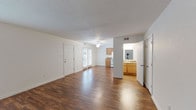 This two-story residence offers a well-organized layout across two levels, combining practical design with comfortable living spaces. The main level features a generously sized living area finished with rich, dark hardwood-style flooring that extends throughout, lending warmth and continuity to the space. Multiple windows allow natural light to fill the room, creating a bright and open atmosphere. A ceiling fan adds functional comfort overhead, while a textured ceiling adds subtle architectural character. The kitchen is efficiently arranged in a galley style, equipped with warm wood cabinetry, dark laminate countertops, white appliances including an electric range, dishwasher, and refrigerator, and a hardwood-style floor that complements the main living area. A half bathroom on the main level provides added convenience. Carpeted stairs lead to the upper level, where two bedrooms are located. The primary bedroom features vaulted ceilings that lend an airy, spacious quality, along with a closet and a window overlooking lush greenery. The second bedroom is comfortably sized with soft carpet flooring and natural light. The full bathroom on the upper level includes a tub-shower combination and hardwood-style flooring.