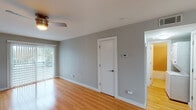 This single-floor residence offers a clean, functional layout with a consistent design language throughout. Warm-toned hardwood flooring flows seamlessly across the living areas, bedroom, and hallways, lending a cohesive and inviting feel to the entire space. The living area is open and well-lit, benefiting from a sliding glass door that allows abundant natural light to pour in, complemented by a ceiling fan overhead for year-round comfort. Neutral gray walls provide a versatile backdrop throughout the home.

The kitchen is outfitted with sleek white cabinetry featuring glass-panel upper doors and brushed nickel hardware, paired with a stainless steel sink and dishwasher. Built-in open shelving adds convenient storage, while the light countertops keep the space feeling bright and functional.

The bedroom is a comfortable, well-proportioned room with its own ceiling fan, a closet with built-in shelving, and a window that brings in natural light. A door from the bedroom provides direct access to the laundry area, where a stacked washer and dryer unit is conveniently housed.

The bathroom features bold golden-yellow tile work on both the floor and tub surround, creating a distinctive retro aesthetic, and includes a full bathtub with shower. The overall ambiance of the space is clean, practical, and move-in ready.