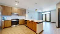 This single-floor residence presents a thoughtfully designed open-concept layout with consistent light wood flooring throughout the main living areas. The kitchen serves as the centerpiece of the space, showcasing warm wood-grain cabinetry on both the upper and lower levels, complemented by clean white countertops and a white subway tile backsplash. A substantial island with an integrated sink and pendant lighting above provides both additional workspace and a natural division between the kitchen and living area. Stainless steel appliances, including a Whirlpool range, refrigerator with ice maker, dishwasher, and built-in microwave, complete the well-equipped kitchen.

The living area benefits from natural light through a large window and a glass door that leads to an outdoor area, with a ceiling fan overhead enhancing comfort. The bedroom features plush carpeting, a ceiling fan, and a window with outdoor views. The bathroom includes accessible design elements such as grab bars near the toilet and bathtub, a single-sink vanity with wood cabinetry, and light wood flooring. A dedicated in-unit laundry closet houses a full-size Whirlpool front-loading washer and dryer with built-in shelving above. Neutral wall tones and recessed lighting contribute to the space's clean, contemporary ambiance.
