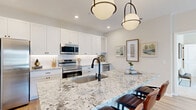 Located at 4985 Warner Rd. in Westerville, Ohio, this well-appointed 2-bedroom, 2-bathroom single-floor residence offers a thoughtfully designed layout that maximizes both comfort and functionality. The open-concept kitchen serves as the centerpiece of the home, showcasing white shaker cabinetry, a striking granite waterfall island with bar seating, stainless steel appliances, a textured tile backsplash, and bold pendant lighting — creating a stylish and highly functional cooking and gathering space. Warm hardwood-style flooring flows throughout the main living areas, lending a cohesive and inviting feel. The living room is bright and welcoming, with multiple windows allowing natural light to fill the space and a glass-panel door providing outdoor access. The spacious primary bedroom features plush carpeting, generous windows with views to the exterior, and access to a walk-in closet outfitted with wire shelving. The second bedroom is equally comfortable, also carpeted and well-lit by natural light. Both bathrooms are finished with granite countertops and hardwood-style flooring. Additional highlights include a dedicated laundry area and four closets total, offering exceptional storage throughout. The neutral color palette and modern finishes create a clean, contemporary ambiance throughout the entire residence.