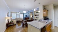 This 2-bedroom, 1-bathroom residence offers a thoughtfully designed open-concept floor plan that maximizes every square foot. The living room serves as the heart of the home, featuring warm hardwood flooring, crown molding, a ceiling fan, and a built-in electric fireplace framed by a rich wood entertainment console. Multiple windows invite abundant natural light, creating a bright and welcoming atmosphere. Vaulted ceilings in a secondary living area add an airy sense of height and openness.

The kitchen is efficiently laid out with warm wood cabinetry, light countertops, a double-basin sink, stainless steel appliances including a refrigerator and range, and track lighting overhead. A kitchen island with a breakfast bar connects seamlessly to the dining area, which features a round wood dining table alongside built-in open shelving — a standout architectural detail that adds both character and display space.

The primary bedroom is a comfortable retreat with carpet flooring, a ceiling fan, and access to a spacious walk-in closet with wire shelving. The second bedroom mirrors a similar calm aesthetic. The shared bathroom includes wood-toned cabinetry, a single-sink vanity, and a shower-tub combination. Throughout, the space maintains a cohesive, neutral palette that feels both practical and inviting.
