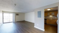 This 2-bedroom, 1.5-bathroom residence is thoughtfully laid out across a single floor, offering a comfortable and functional living environment. The open living area serves as the heart of the home, showcasing rich, dark hardwood-style flooring that runs throughout and provides a warm, grounded aesthetic. The space is finished with clean white walls and a textured ceiling, lending a classic, understated character to the interior. A wall-mounted air conditioning unit and baseboard heating ensure year-round climate control and comfort. A built-in electrical panel is conveniently recessed into the wall, maintaining a tidy, organized appearance. Natural light filters into the living area, complementing the neutral color palette and creating a bright, welcoming atmosphere. Adjacent to the main living space, the kitchen is visible and appears to feature warm cabinetry, adding a touch of coziness to the layout. The unit's two bedrooms offer private retreats, while the 1.5 bathrooms provide practical convenience for residents and guests alike. Overall, this unit delivers a clean, move-in-ready living experience with essential amenities thoughtfully integrated throughout.