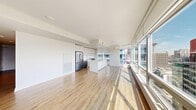Located in the heart of Calgary, this modern 3-bedroom, 2-bathroom unit showcases a bright and contemporary design throughout. The open-concept living and kitchen area is immediately impressive, anchored by expansive floor-to-ceiling windows that flood the space with natural light and frame sweeping views of the Calgary skyline and surrounding cityscape. Light hardwood flooring runs seamlessly throughout, complementing the clean white walls and modern finishes.

The kitchen is thoughtfully designed with sleek white cabinetry extending to the ceiling, a large central island with a white quartz countertop, stainless steel appliances including a gas range and French door refrigerator, and recessed lighting overhead. The open layout allows the kitchen to flow effortlessly into the living area, making it ideal for entertaining.

A long, well-lit hallway with track lighting and a stylish sliding barn door leads to the three bedrooms. Each bedroom benefits from natural light and city views through generous windows. The primary bedroom offers a private, comfortable retreat.

Both bathrooms are finished in a clean, minimalist style, featuring large-format tile flooring, white cabinetry with integrated sinks, and a full tub-shower combo with a glass enclosure. Every detail of this unit reflects a cohesive modern aesthetic, making it a polished urban residence in Calgary's vibrant core.