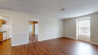 Located at 215 McMillan Ave in Bay Minette, Alabama, this single-story, 2-bedroom, 2-bathroom home offers a practical and comfortable layout. Rich hardwood-style flooring flows consistently throughout the entire home, complemented by crown molding and textured ceilings that add a classic touch to every room.

The living room is generously sized, offering an open and airy feel with neutral wall tones that create a bright, welcoming atmosphere. It connects seamlessly to the galley-style kitchen, which features warm wood cabinetry, dark countertops, and white appliances including a range, dishwasher, and refrigerator. A ceiling fan light fixture illuminates the kitchen area, which also includes a wood-paneled accent wall for added character.

The primary bedroom is spacious and well-lit, benefiting from a large window that allows natural light to fill the room. The second bedroom also features a ceiling fan and a window with views of the surrounding area. Both rooms offer ample space for comfortable living.

The two bathrooms each include a tub-shower combination. One bathroom features a white vanity with a marble-style countertop and louvered storage shelving, while the other includes a white vanity and clean, simple finishes. A hallway and closet round out the home's functional layout.
