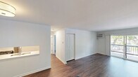 Located at 1049 S Main St in Crown Point, Indiana, this one-bedroom, one-bathroom unit offers a well-organized single-floor layout with a clean, modern aesthetic throughout. The living room is a standout space, featuring rich hardwood-style flooring, a wall-mounted air conditioning unit, and a baseboard heating system. Large sliding glass doors open directly onto a private balcony with a railed deck, allowing generous natural light to fill the room and providing pleasant outdoor views of surrounding greenery. The entry area continues the hardwood-style flooring and connects seamlessly to the rest of the unit, with a pass-through detail offering a glimpse into the kitchen. The kitchen area is outfitted with light-toned walls and hardwood-style flooring, maintaining a cohesive look with the main living spaces. The bedroom is a comfortable, well-proportioned room finished with soft wall-to-wall carpeting, a closet, a window with natural views, and baseboard heating. The bathroom features a clean, bright design with light tile flooring, white subway tile surrounding the tub and shower combination, and a sliding glass shower enclosure. Throughout the unit, crisp white walls and consistent trim work contribute to a fresh, move-in-ready atmosphere.