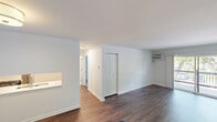 Located at 1049 S Main St in Crown Point, Indiana, this one-bedroom, one-bathroom unit offers a well-organized single-floor layout with a clean, modern aesthetic throughout. The living room is a standout space, featuring rich hardwood-style flooring, a wall-mounted air conditioning unit, and a baseboard heating system. Large sliding glass doors open directly onto a private balcony with a railed deck, allowing generous natural light to fill the room and providing pleasant outdoor views of surrounding greenery. The entry area continues the hardwood-style flooring and connects seamlessly to the rest of the unit, with a pass-through detail offering a glimpse into the kitchen. The kitchen area is outfitted with light-toned walls and hardwood-style flooring, maintaining a cohesive look with the main living spaces. The bedroom is a comfortable, well-proportioned room finished with soft wall-to-wall carpeting, a closet, a window with natural views, and baseboard heating. The bathroom features a clean, bright design with light tile flooring, white subway tile surrounding the tub and shower combination, and a sliding glass shower enclosure. Throughout the unit, crisp white walls and consistent trim work contribute to a fresh, move-in-ready atmosphere.
