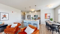 This single-floor residence at 1780 W Orchard Rd in North Aurora, Illinois offers a thoughtfully designed open-concept layout that seamlessly connects the living, dining, and kitchen areas. The kitchen is a standout feature, equipped with stainless steel appliances, white shaker-style cabinetry with gray lower cabinets, a large center island with bar seating, white quartz countertops, and pendant lighting — all set above warm-toned hardwood-style flooring that flows throughout the main living spaces. The dining area is positioned near large windows fitted with horizontal blinds, allowing generous natural light and views of the surrounding greenery. The living room is spacious and bright, with expansive windows that frame outdoor views of trees and open grounds. The bedroom is generously sized, featuring plush carpeting, multiple windows, and a walk-in closet with built-in wire shelving for organized storage. The bathroom is clean and functional, outfitted with a gray vanity, white countertop, wood-look flooring, and a full soaking tub with shower. Throughout, the residence maintains a neutral, contemporary palette that creates a calm and inviting atmosphere well-suited for everyday living.