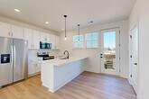 Located at 4418 Oat Grass Circle in Charlotte, NC, this modern three-story townhome offers a well-designed layout across three distinct levels. The ground floor houses an attached garage with a window for natural light, plus a welcoming entrance hallway finished with light hardwood-style flooring and clean white walls accented by matte black hardware.

The main living level serves as the heart of the home, combining the kitchen, dining, and living areas in one bright, open-concept space. The kitchen is a standout feature, showcasing white shaker cabinetry, a quartz waterfall island with a black matte faucet, stainless steel appliances including a French door refrigerator, a tiled backsplash, and stylish pendant lighting. A glass door opens to a private balcony, inviting natural light and outdoor views.

The upper floor hosts all three bedrooms, each featuring light hardwood flooring, crisp white walls, ample closet space with wire shelving, and windows that bring in generous natural light. The primary bedroom is a comfortable retreat with access to walk-in closet storage. The four bathrooms are outfitted with dual-sink white vanities, quartz countertops, and matte black fixtures, maintaining the home's consistent modern aesthetic. A dedicated laundry area and pantry add practical convenience throughout.