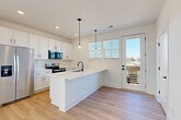 Located at 4418 Oat Grass Circle in Charlotte, NC, this modern three-story townhome offers a well-designed layout across three distinct levels. The ground floor houses an attached garage with a window for natural light, plus a welcoming entrance hallway finished with light hardwood-style flooring and clean white walls accented by matte black hardware.

The main living level serves as the heart of the home, combining the kitchen, dining, and living areas in one bright, open-concept space. The kitchen is a standout feature, showcasing white shaker cabinetry, a quartz waterfall island with a black matte faucet, stainless steel appliances including a French door refrigerator, a tiled backsplash, and stylish pendant lighting. A glass door opens to a private balcony, inviting natural light and outdoor views.

The upper floor hosts all three bedrooms, each featuring light hardwood flooring, crisp white walls, ample closet space with wire shelving, and windows that bring in generous natural light. The primary bedroom is a comfortable retreat with access to walk-in closet storage. The four bathrooms are outfitted with dual-sink white vanities, quartz countertops, and matte black fixtures, maintaining the home's consistent modern aesthetic. A dedicated laundry area and pantry add practical convenience throughout.